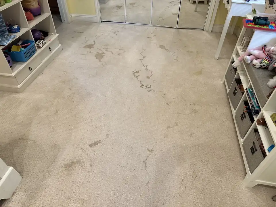 Beige cut-pile carpet in a kids' room before cleaning, blotchy spots and stains across the floor beside white cubbies