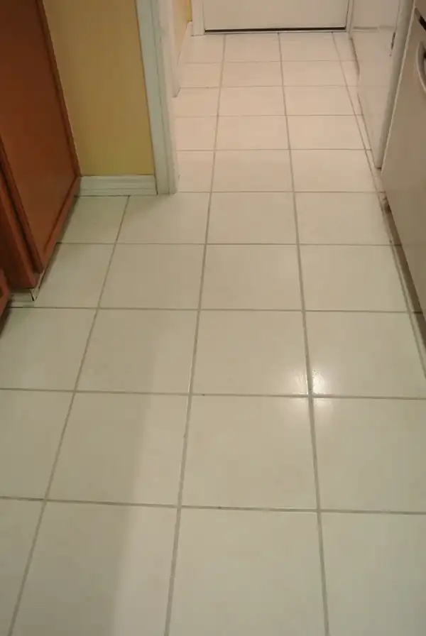 Cream ceramic tile down a galley kitchen with clean, even grout lines